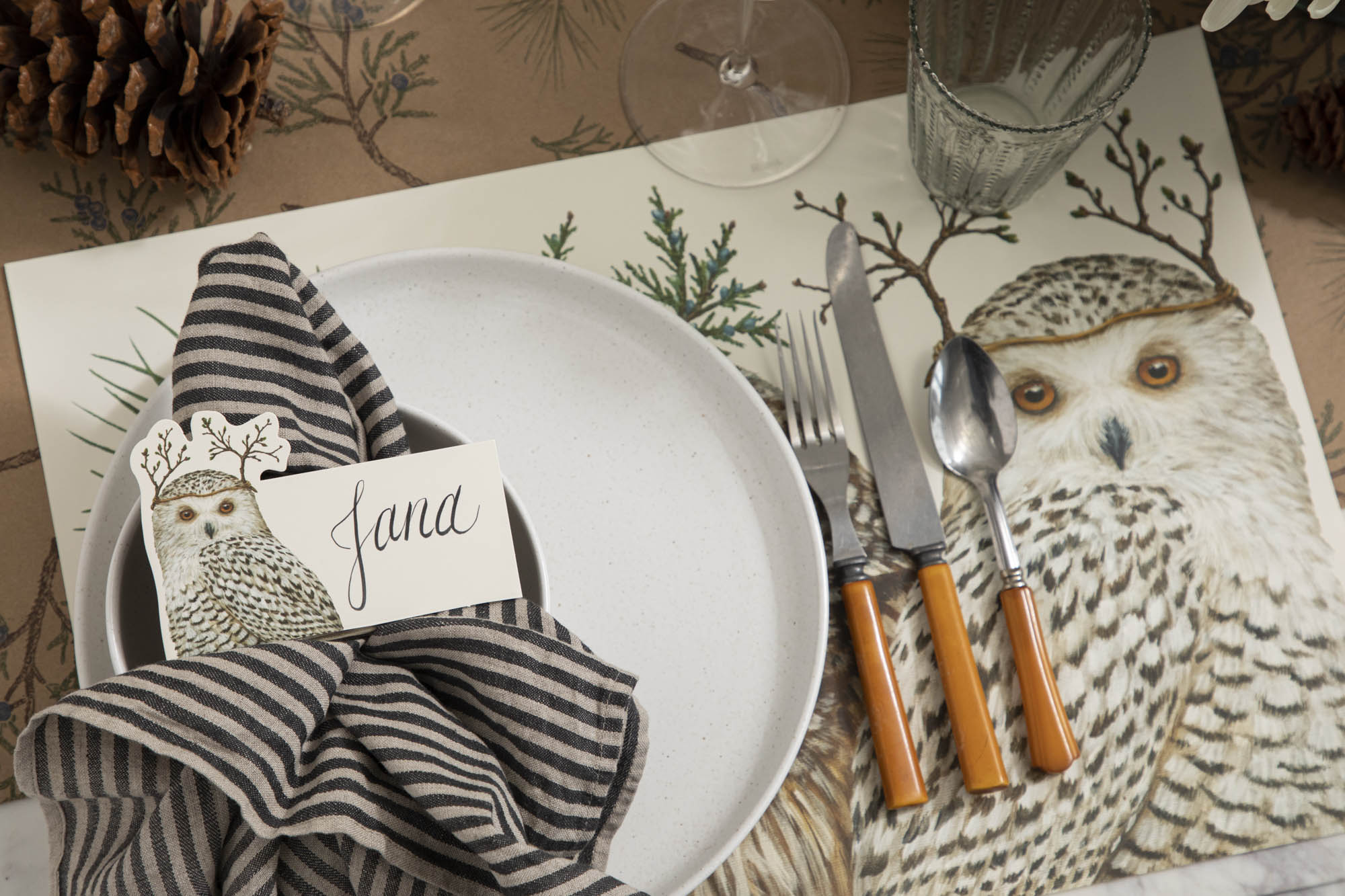 Place setting featuring a patterned white plate with the Evergreen place card reading "Julie" on top of another white plate with the Evergreen Forest Placemat and Juniper Sprigs Runner underneath.