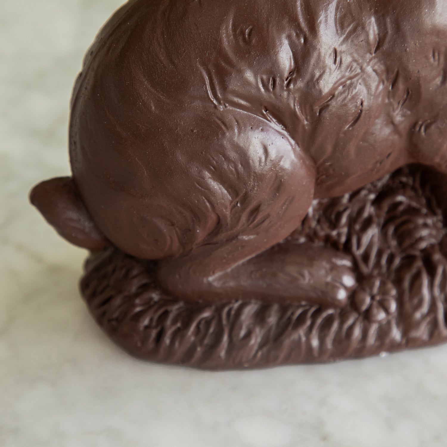 A close up of the &quot;Chocolate&quot; Sitting Bunny showing its feet on the grass.