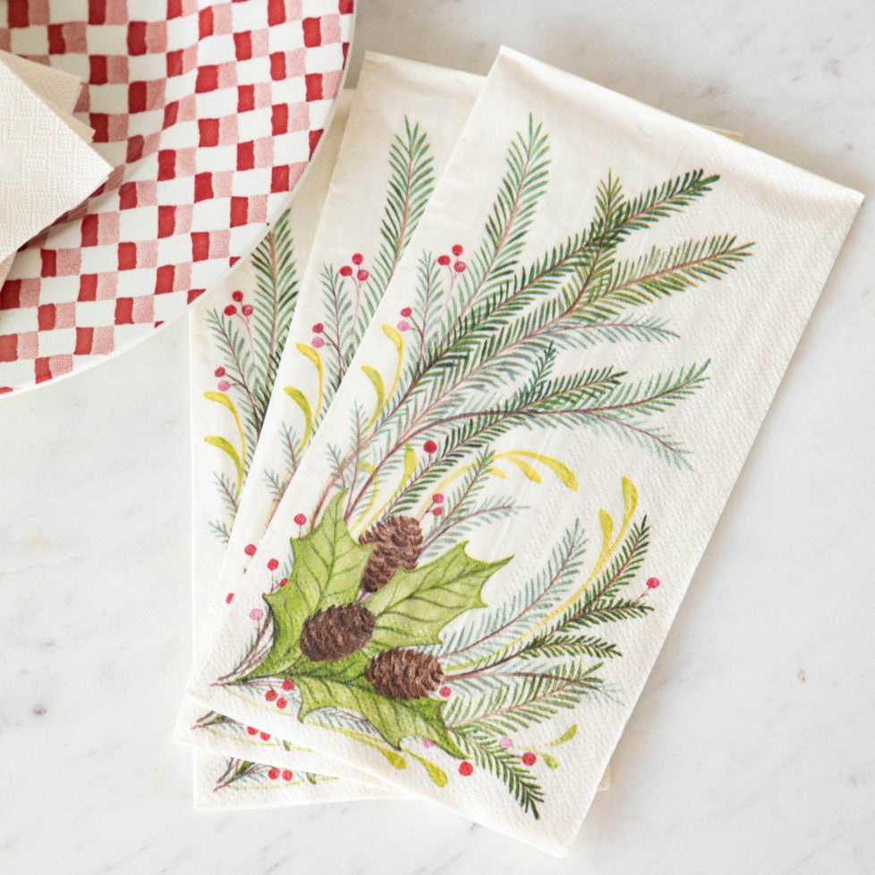 Three Christmas Sprigs Guest Napkins fanned out on a table next to a red and white plate.