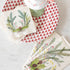 A top-down view of a table with a stack of Christmas Sprigs Cocktail Napkins and a stack of Christmas Sprigs Guest Napkins, fanned out next to a red and white plate and a cup of hot chocolate.