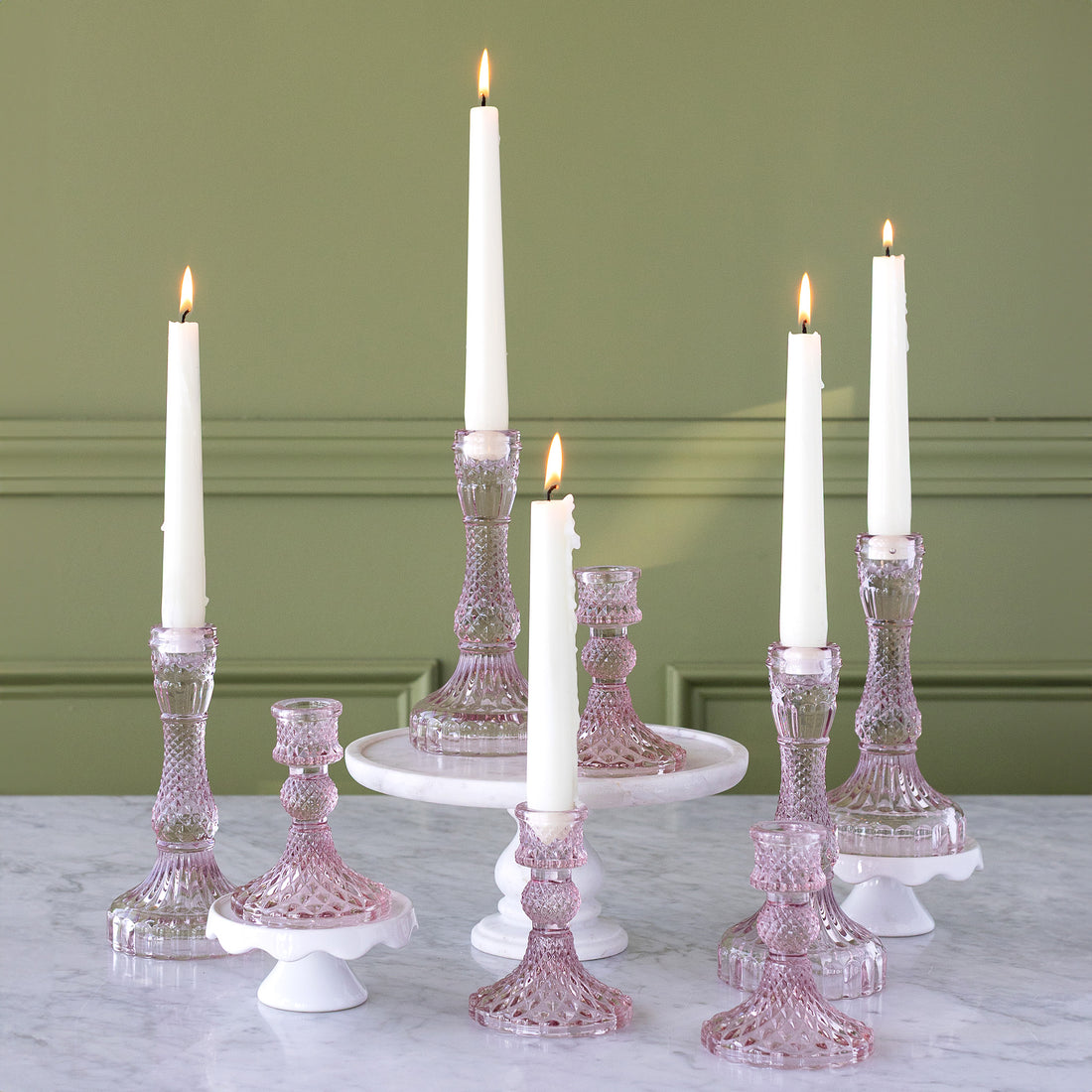 Short and Tall Vintage Pink Candlesticks on a table with lit candles in them.