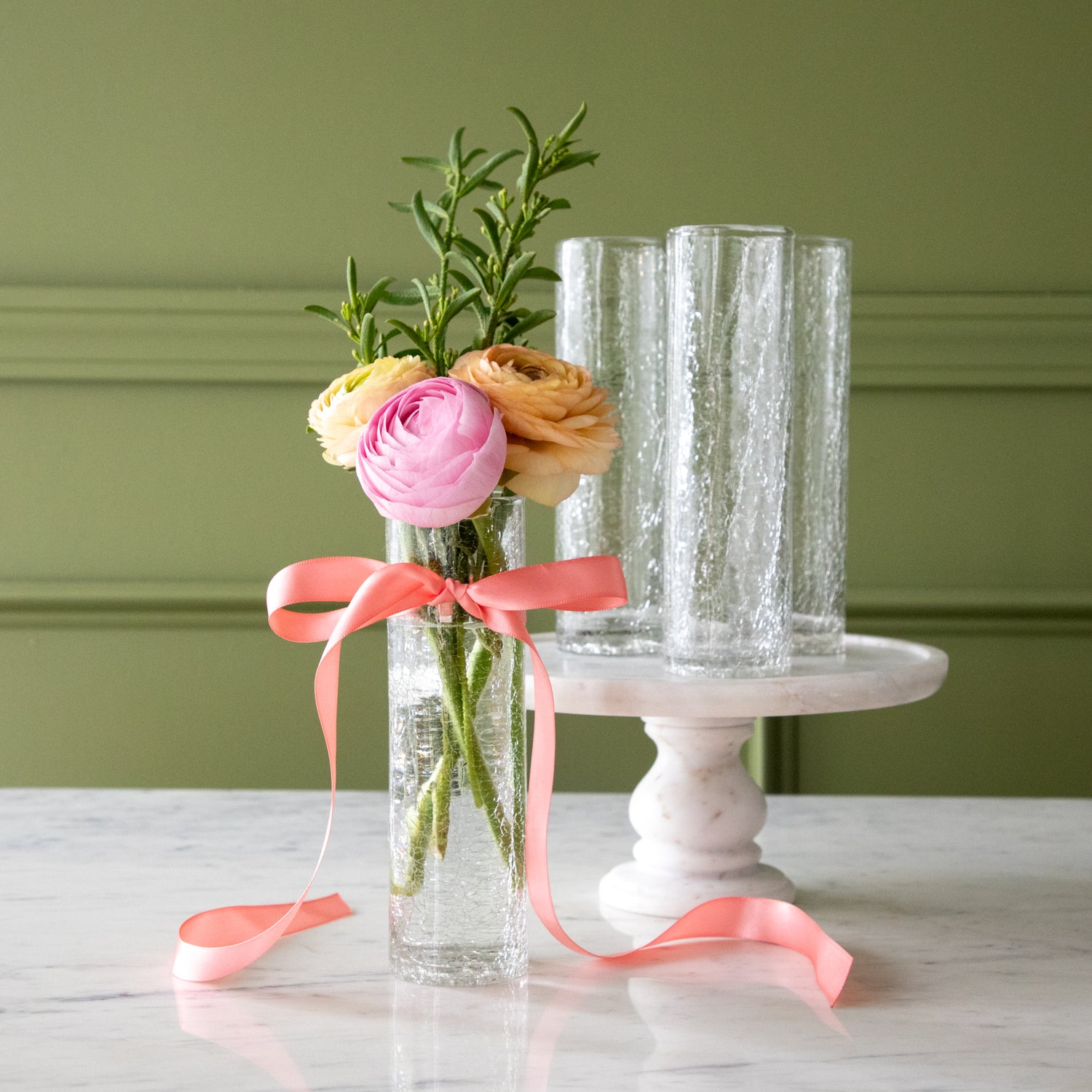 Three Norwell Champagne Flutes on a pedestal and one on the table with flowers in it and a pink bow tied around it.