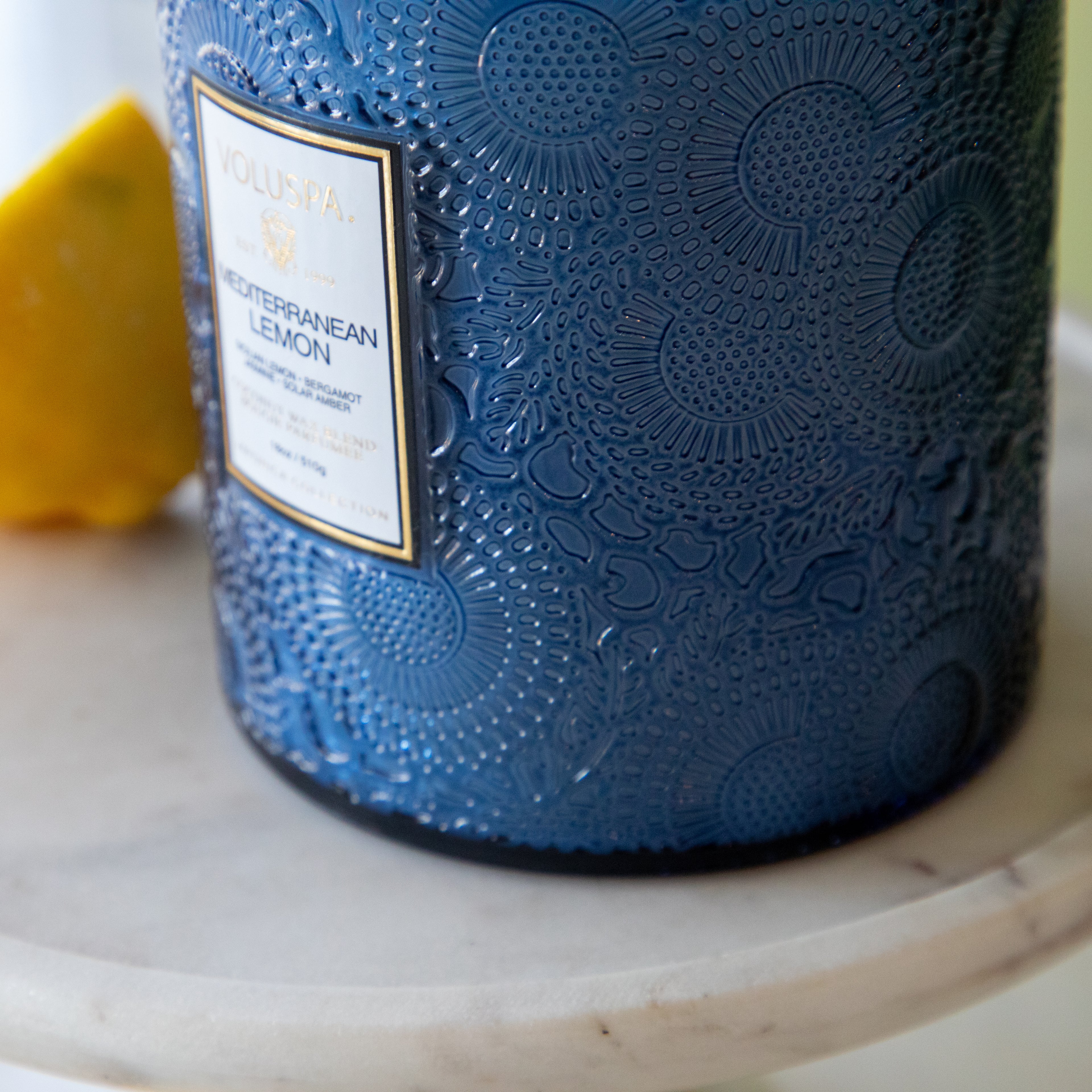 A close up of the Large Mediterranean Lemon Candle showing its swirled and circular designs in the blue glass.