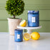 Small and large Mediterranean Lemon Candles surrounded by lemons with boxwood topiary in the background.