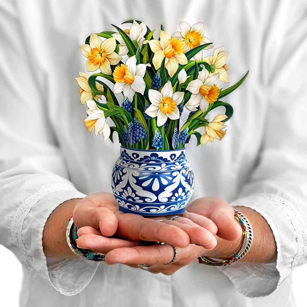 A potted arrangement of artificial orchids with a wooden stand against a white background, accompanied by a Fresh Cut Paper Mini Pop Up Flower Bouquet.