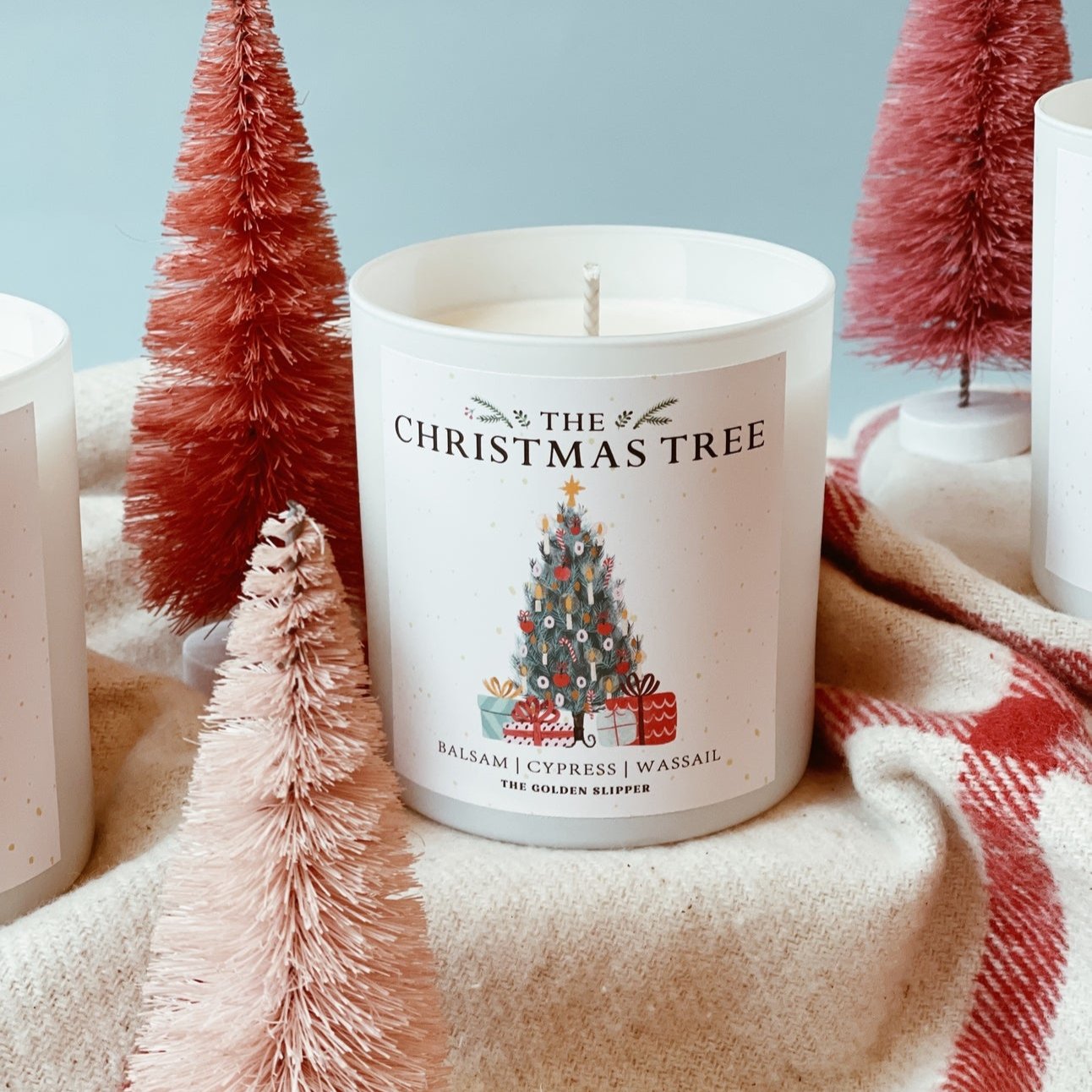 The Christmas Tree Candle surrounded by mini trees, on top of a blanket, made by The Golden Slipper.