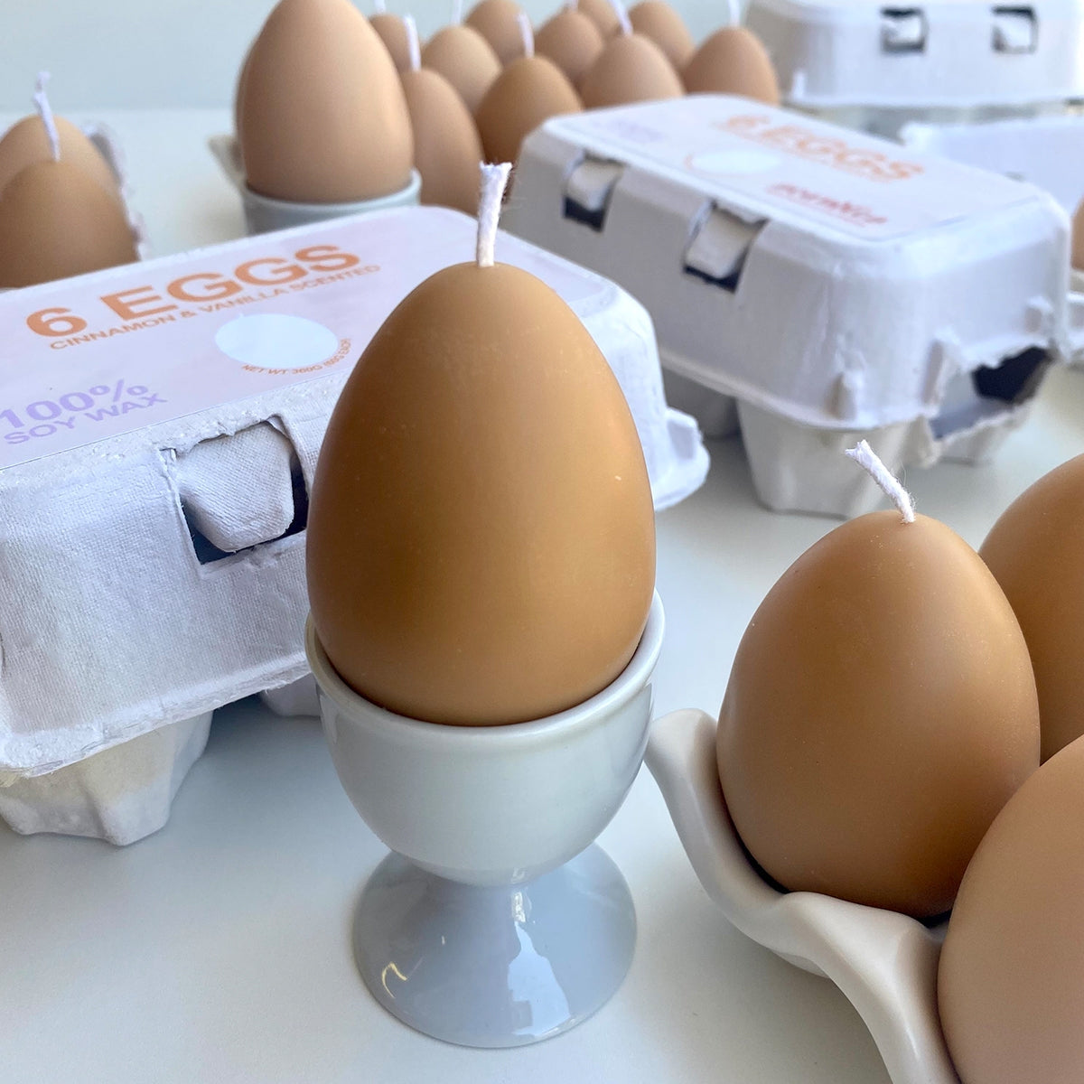 Close up of egg candle in a cup in foreground and 2 cartons of egg candles in the background. 