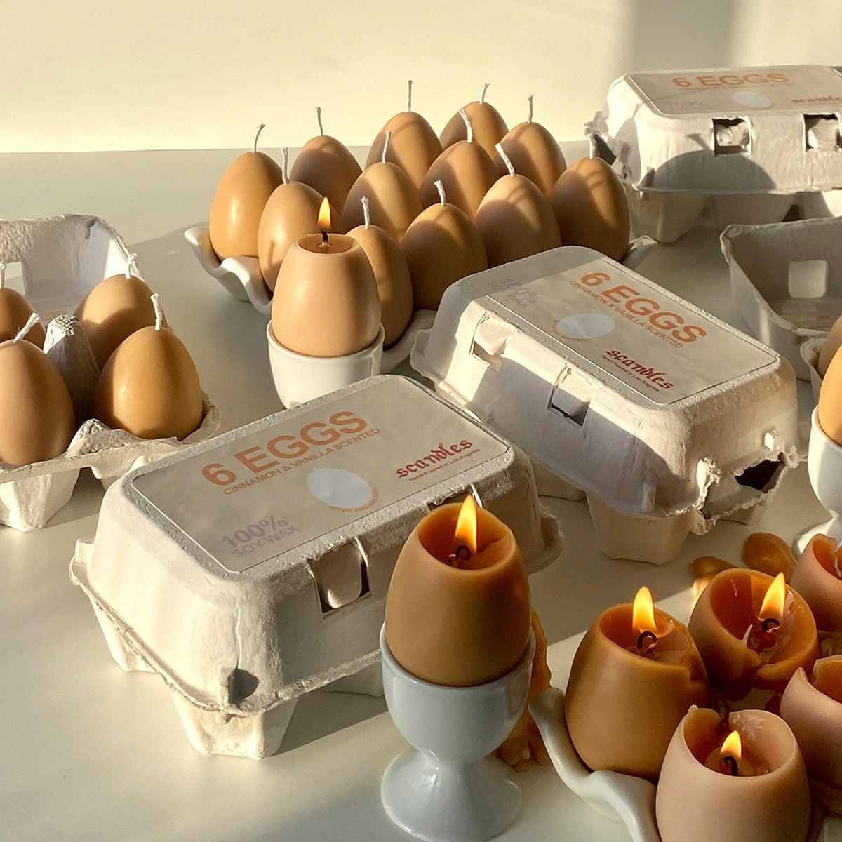 Egg candles burning in egg cups with open and closed boxes of egg candles. 