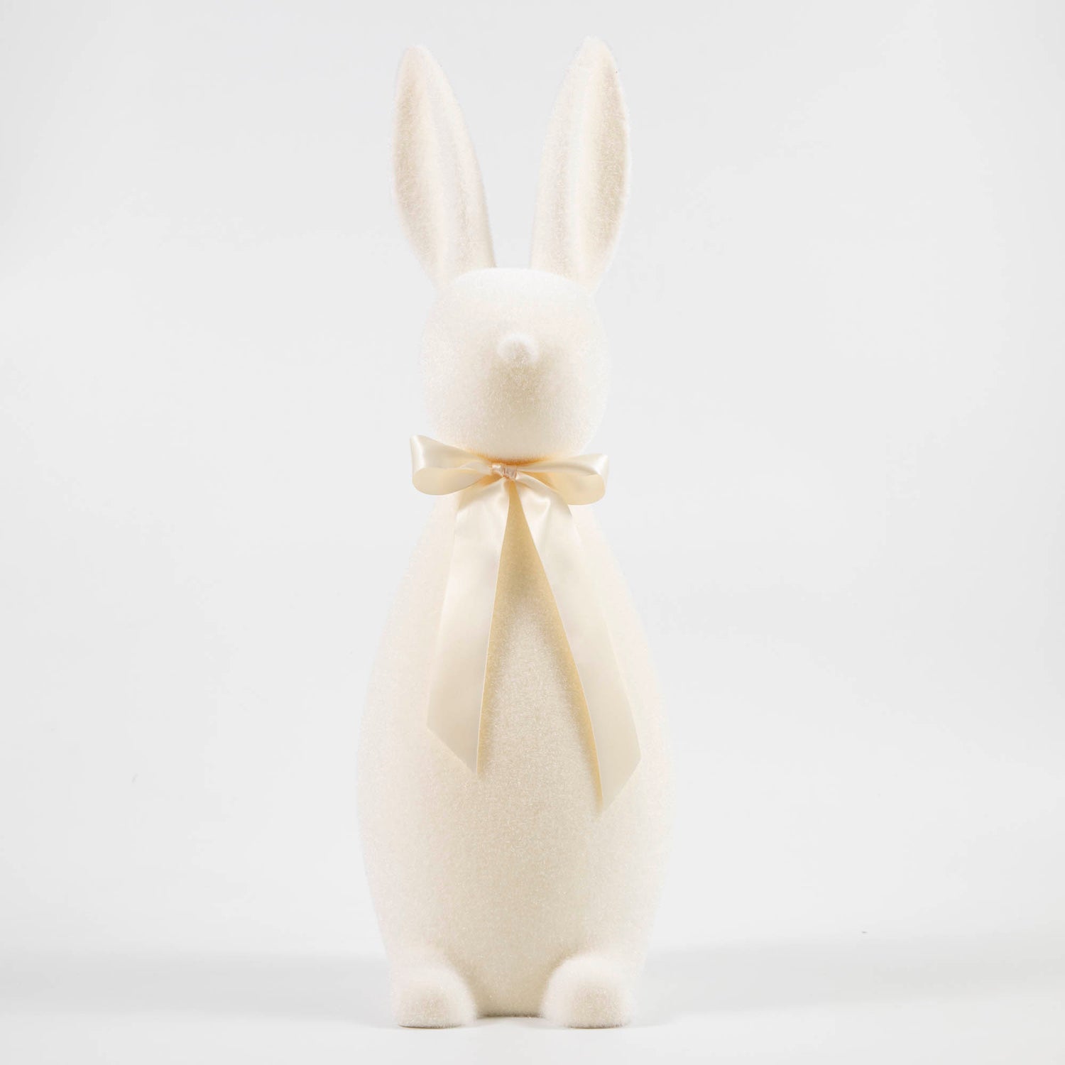 White flocked bunny with a pink bow tied around its neck. 