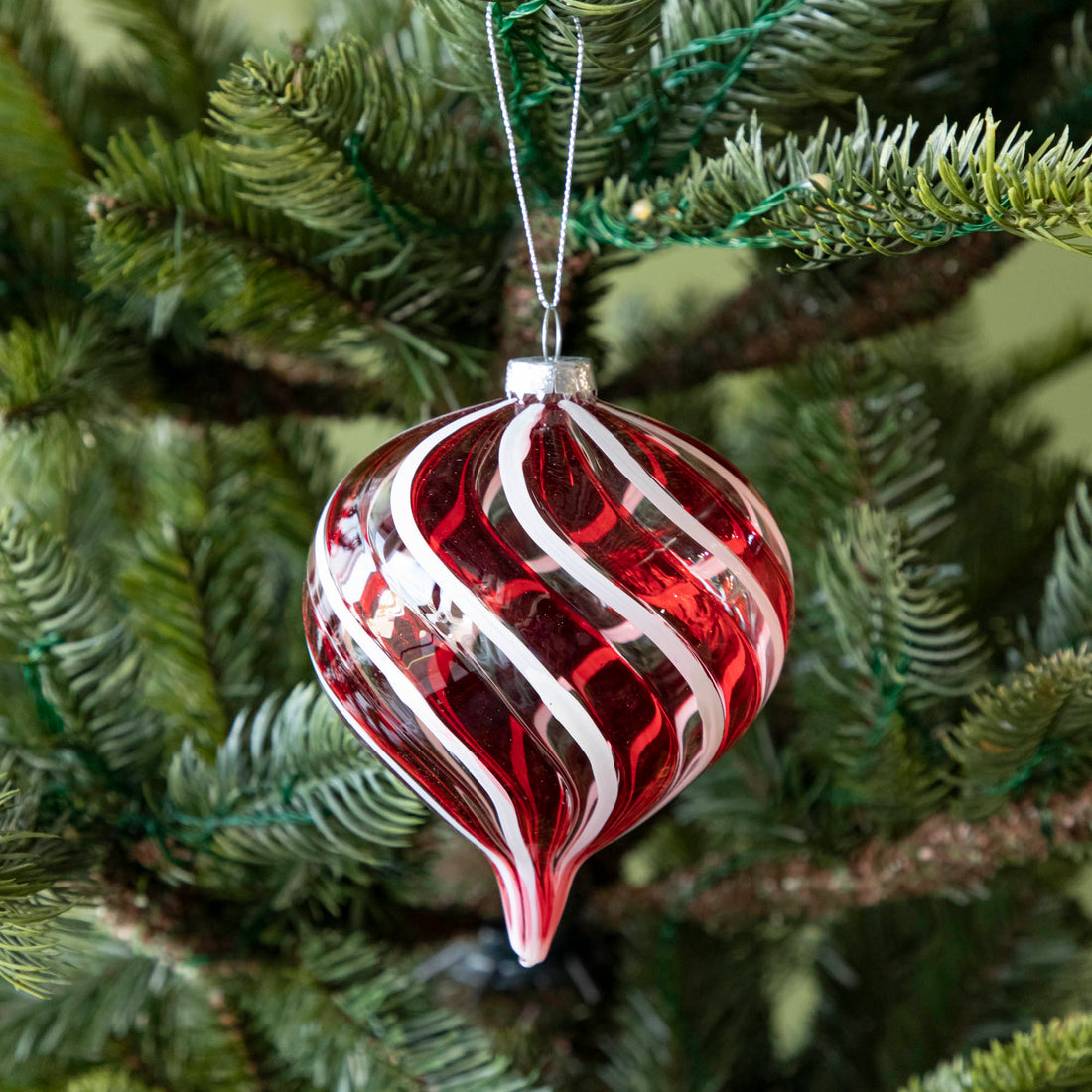 A long Peppermint Stripe Ornament hanging on a tree by a silver string.