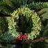 A 5" acrylic green wreath ornament with silver accents, bright red berries and a red bow, hanging on a tree by a silver string.