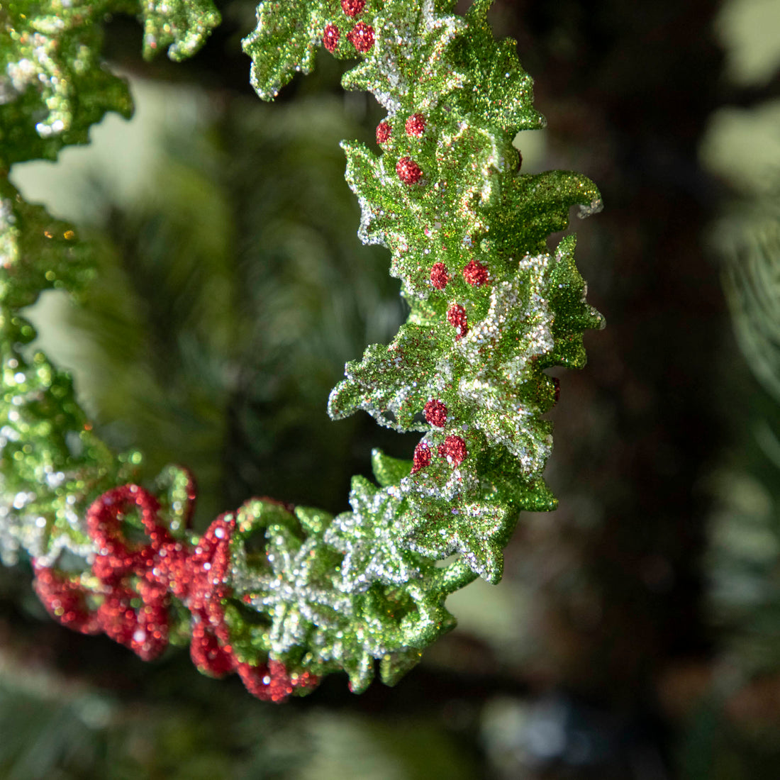 A  close up of the green wreath ornament showing its silver accents, bright red berries and a red bow.