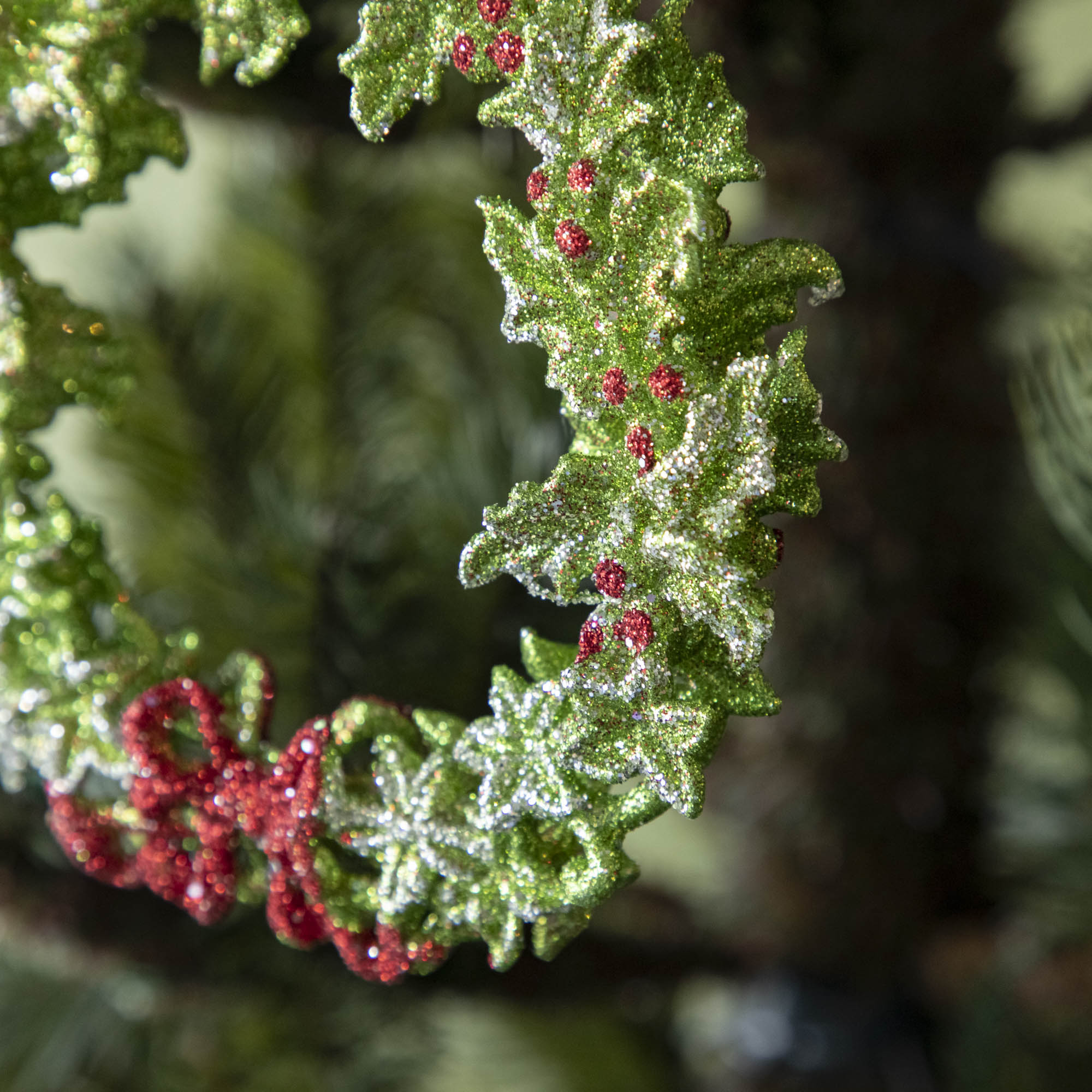 A  close up of the green wreath ornament showing its silver accents, bright red berries and a red bow.