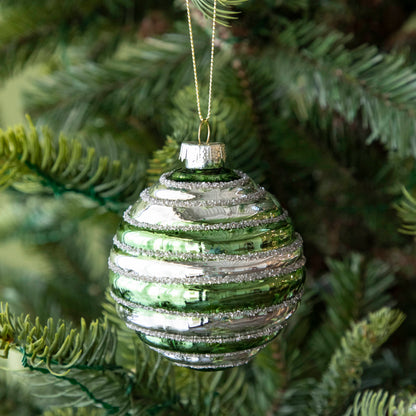 A Glass Silver Stripe Ball Ornament with green stripes and silver glitter, hanging on a tree by a gold string.