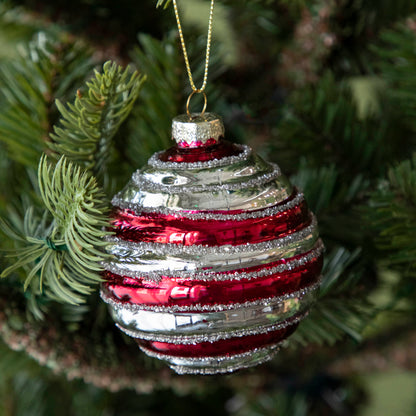 A Glass Silver Stripe Ball Ornament with red stripes and silver glitter, hanging on a tree by a gold string.