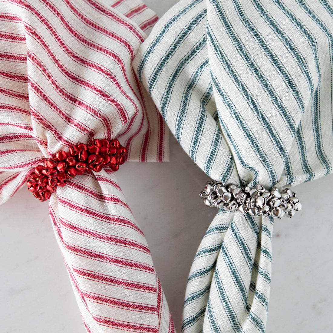 A silver and red Petite Bell Napkin ring holding a stripe napkin.