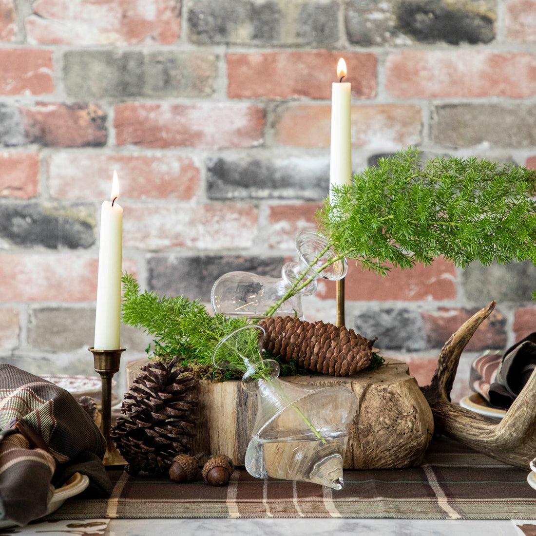 A table adorned with small bouquets of flowers in the Mouth Blown Clear Vase - Exclusively at Hester &amp; Cook, alongside candles and pine cones.