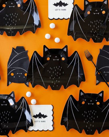 Overhead shot of bat shaped paper plates and napkins on an orange background.