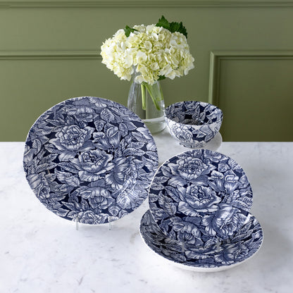 Burleigh Ink Blue Hibiscus Dinnerware propped up with a vase of flower behind them.