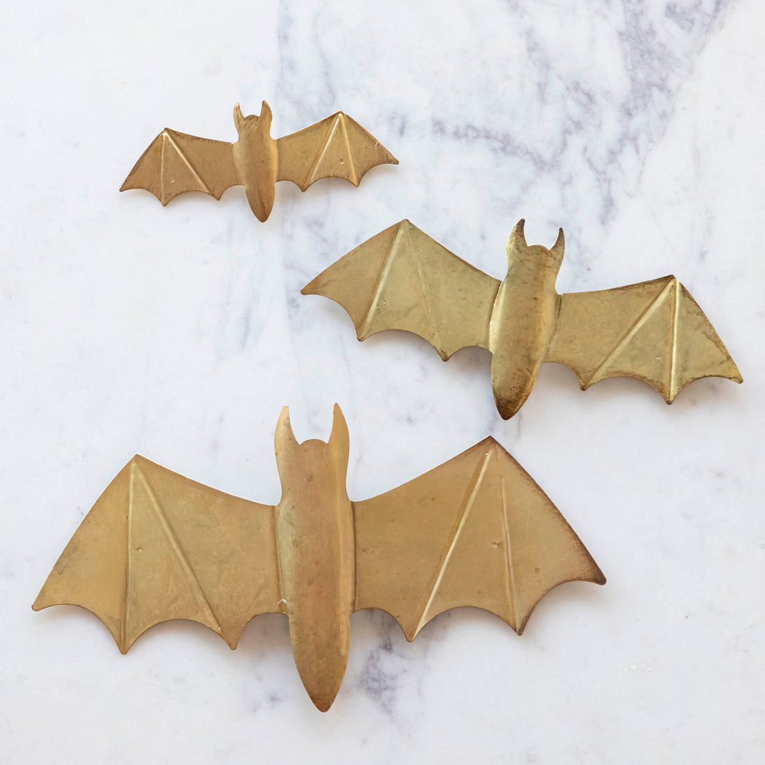 A small, medium and large metal winged bat on marble.