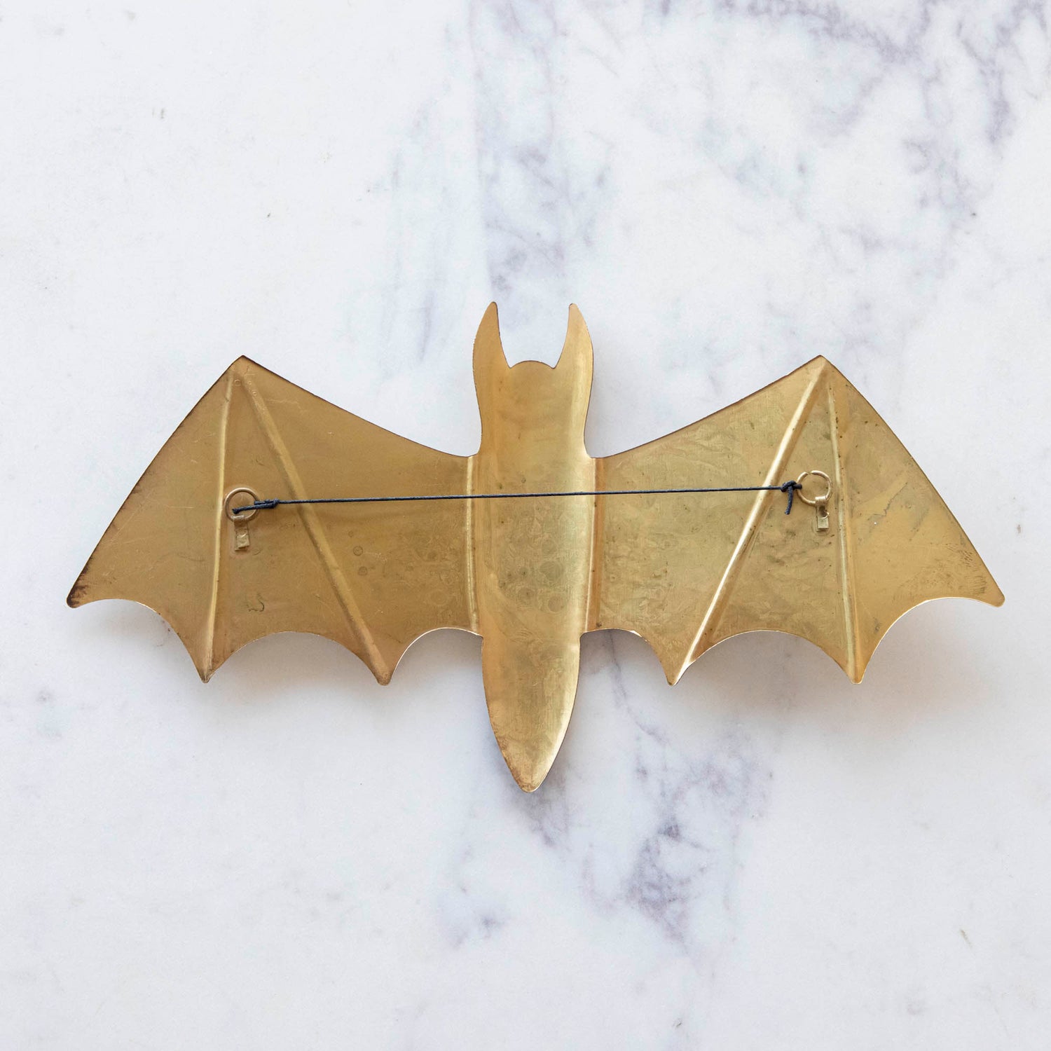 A back view of a large metal winged bat featuring a string for hanging.