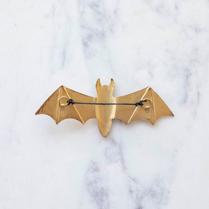 A back view of a small metal winged bat featuring a string for hanging.