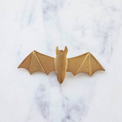 A small, gold metal winged bat on marble.