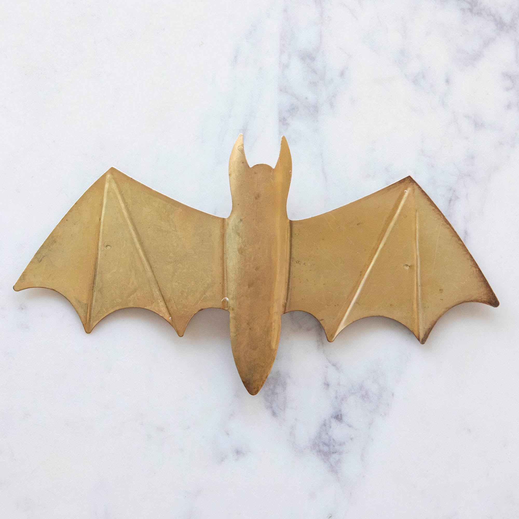 A medium, gold metal winged bat on marble.