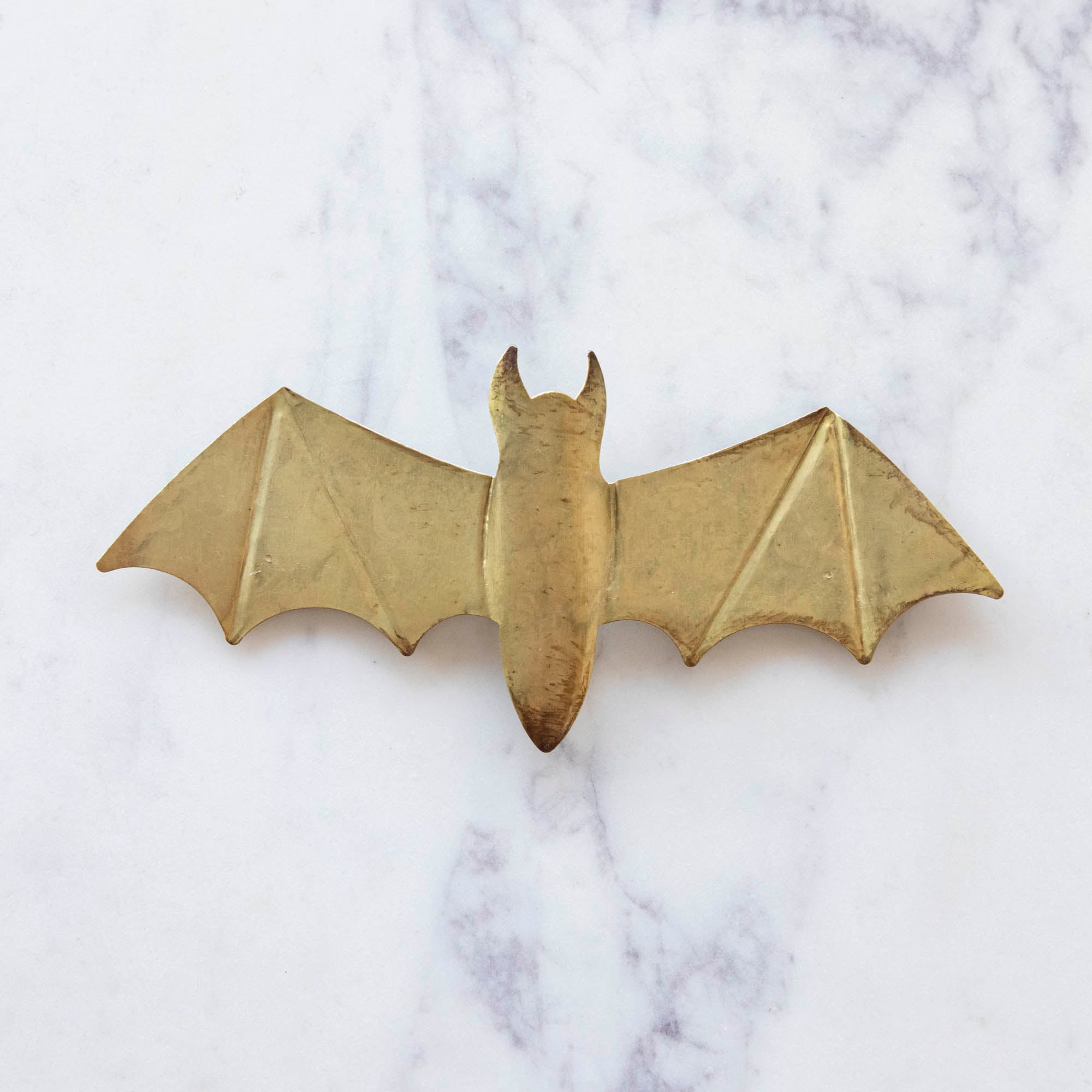 A medium, gold metal winged bat on marble.