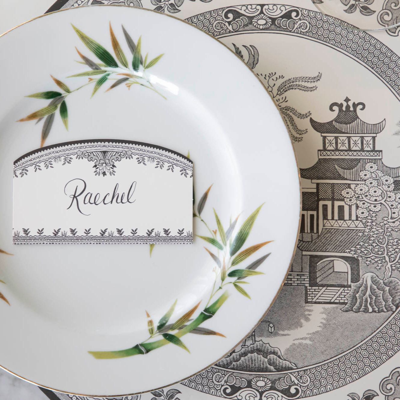 Black Willow Place Card with &quot;Raechel&quot; written on it, resting on a dinner plate on top of the Die-cut Black Willow Placemat.