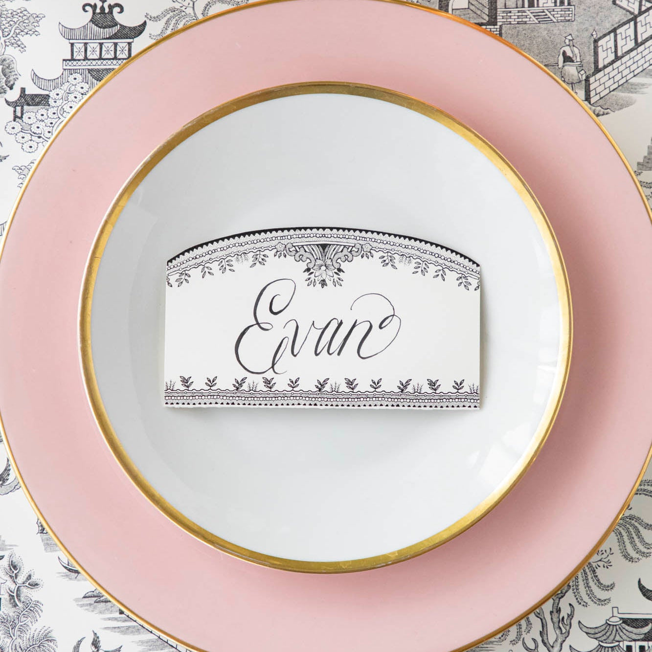 Black Willow Place Card with &quot;Evan&quot; written on it, resting on dinner plates on an elegant place setting.