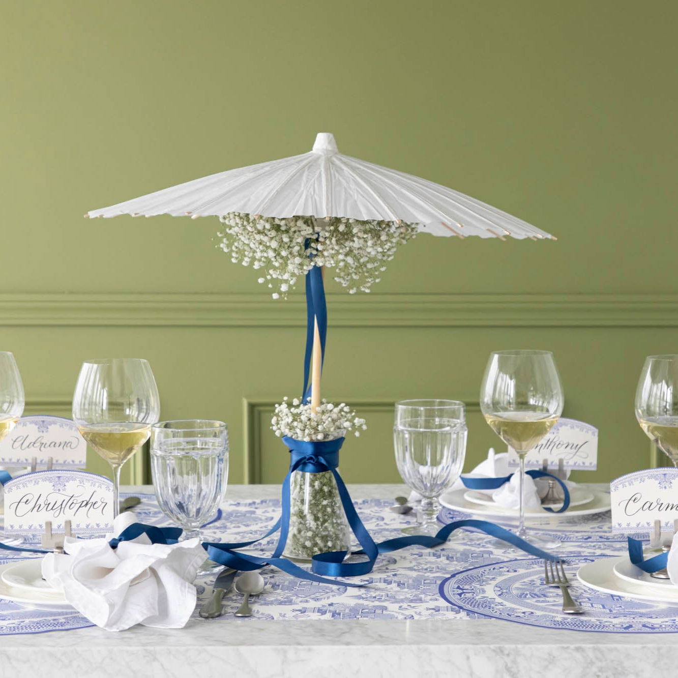 The Die-cut Blue Willow Plate Placemat elegantly styled on a dinner table for four, with an umbrella fan in a jar with flowers.