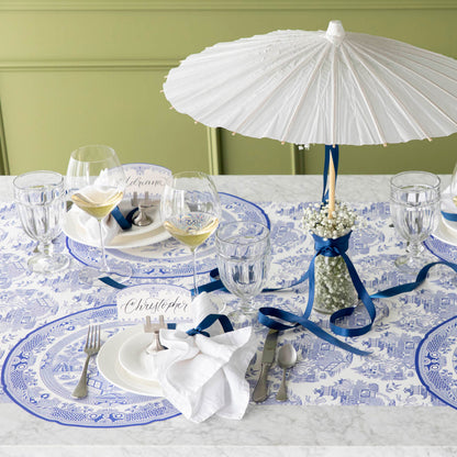 The Die-cut Blue Willow Plate Placemat elegantly styled on a dinner table for four, with an umbrella fan in a jar with flowers.