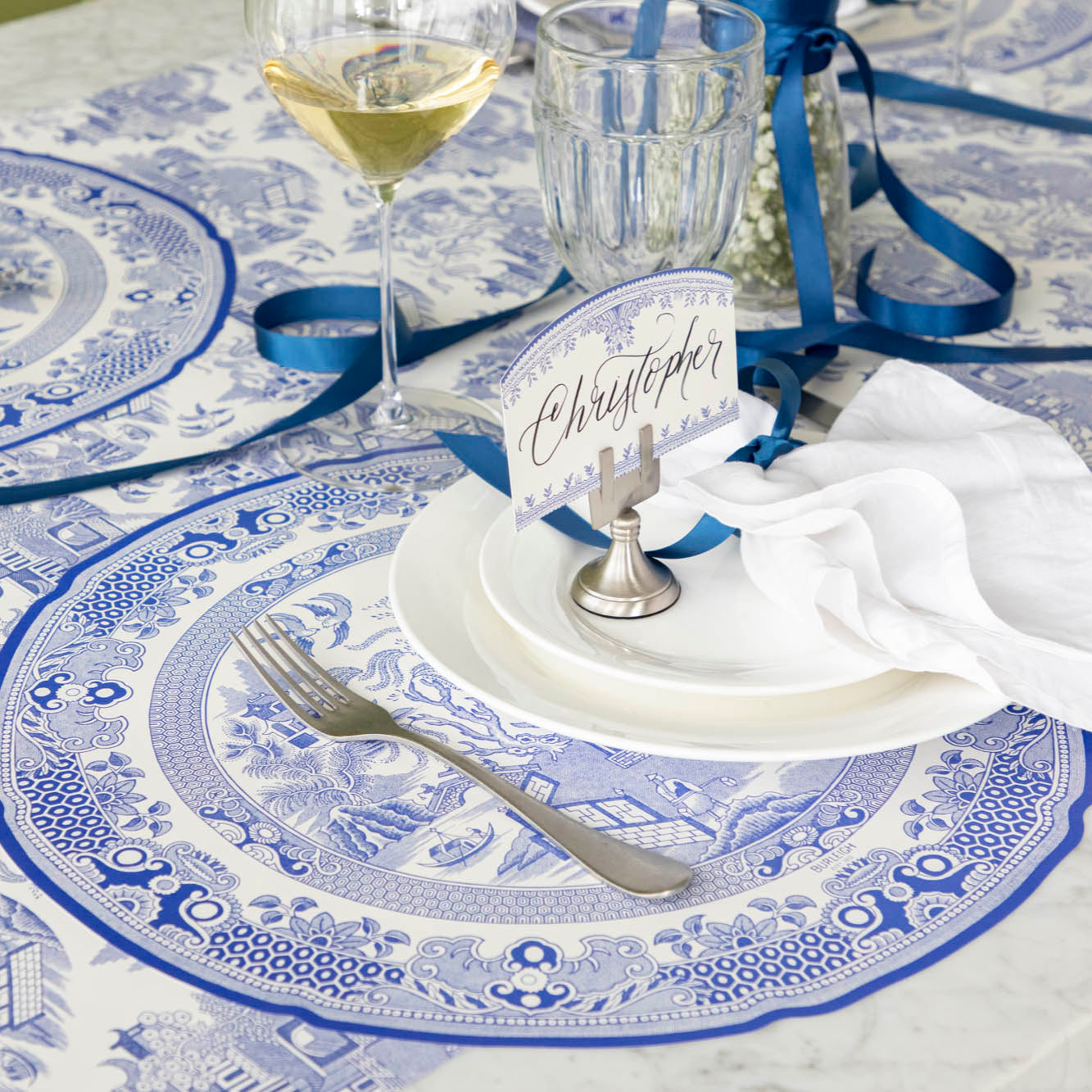 Die-cut Blue Willow Plate Placemat elegantly paired with white dinnerware and a vintage silver fork on top.