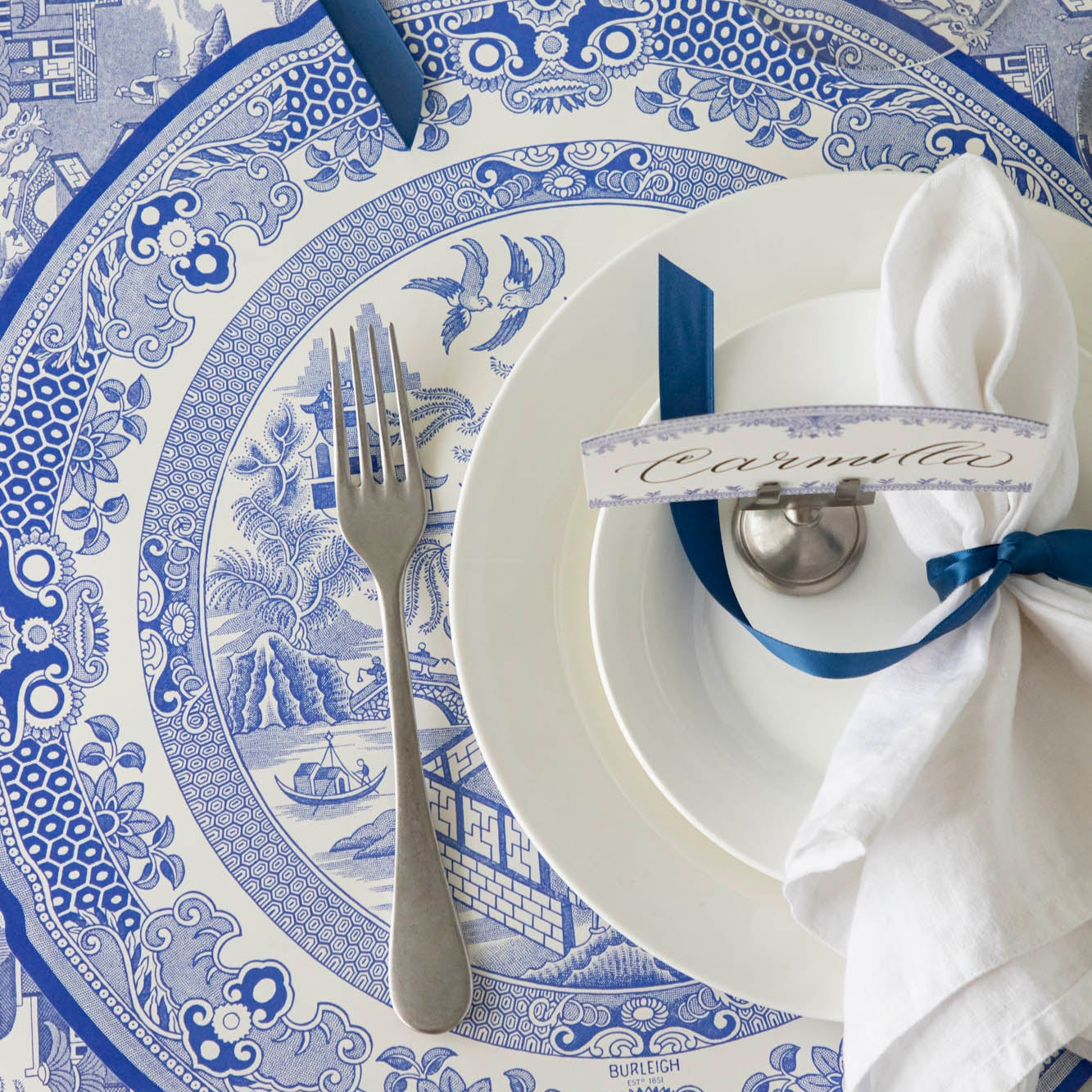 Die-cut Blue Willow Plate Placemat elegantly paired with white dinnerware and a vintage silver fork on top.