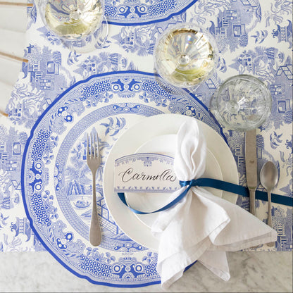 Burleigh Blue Place Card with &quot;Camilla&quot; written in the white space, resting on dinner plates, on top of the Die-cut Blue Willow Plate Placemat. 