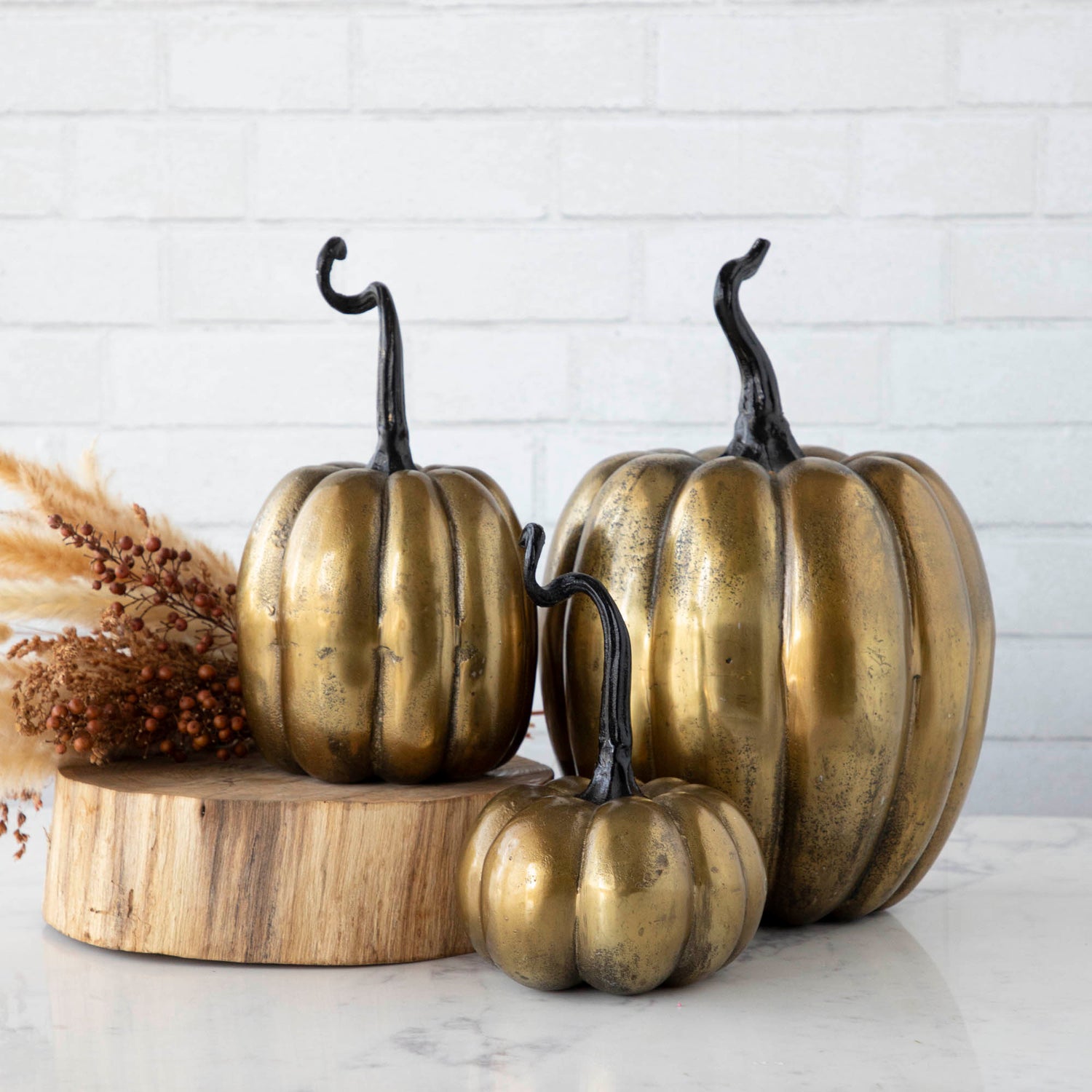 Three handmade Accent Decor brass pumpkins on a wooden table.