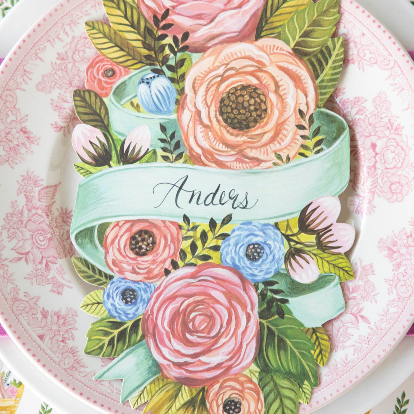 Spring Floral Table Accent with &quot;Anders&quot; written on it, resting in the center of dinner plates on a place setting for one.