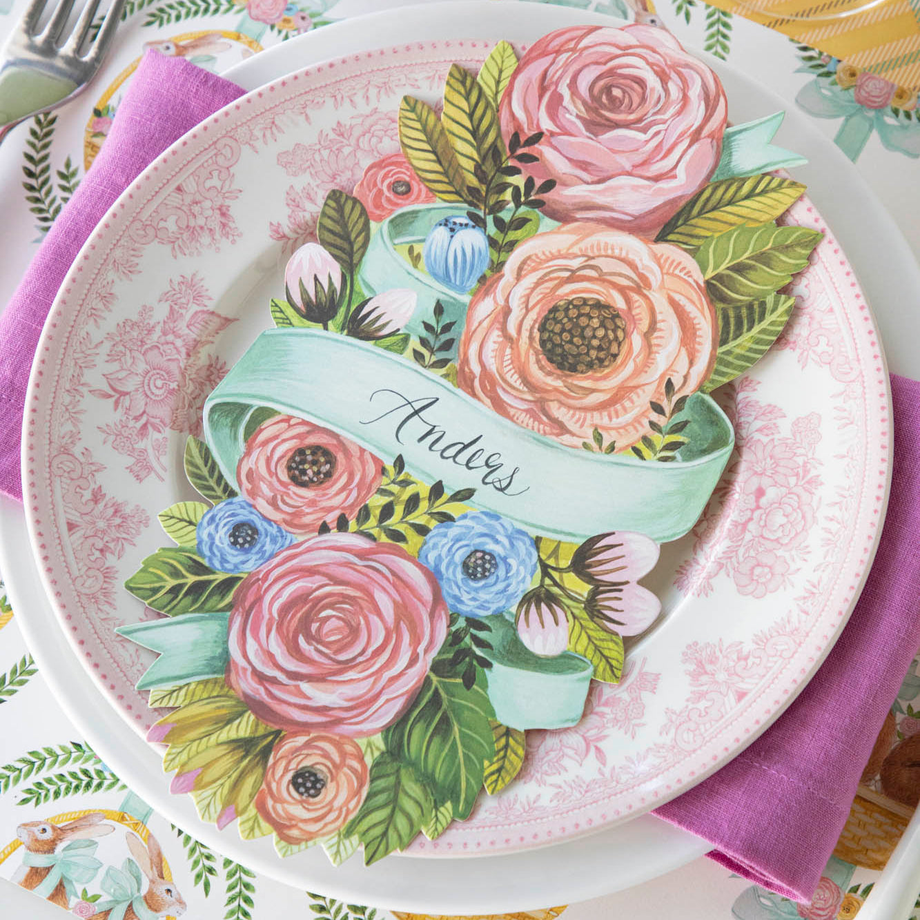 Spring Floral Table Accent with &quot;Anders&quot; written on it, resting in the center of dinner plates on a place setting for one.