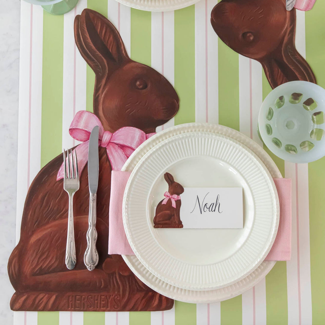 Die-cut Hershey's Chocolate Bunny Placemat on the Green & Pink Awning Stripe Runner, with a place setting for one on top.