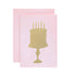 A light pink card with the silhouette of a birthday cake on a stand in solid gold leaf.