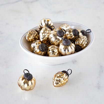 A white bowl on a marble table filled with one inch Embossed Antique Gold Mercury Glass Ornaments and two outside of the bowl.