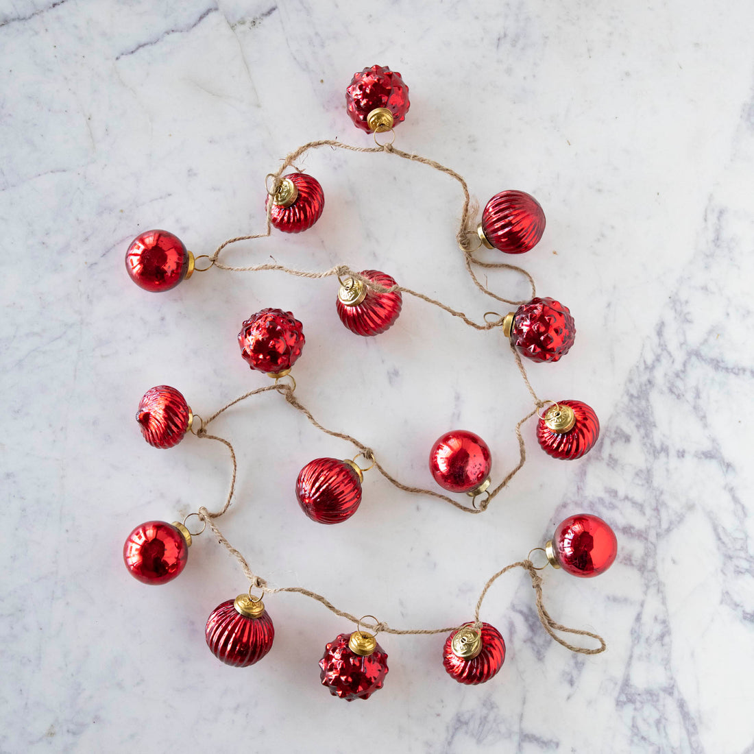 Embossed Red Mercury Glass Ball Ornament Garland on a marble table.