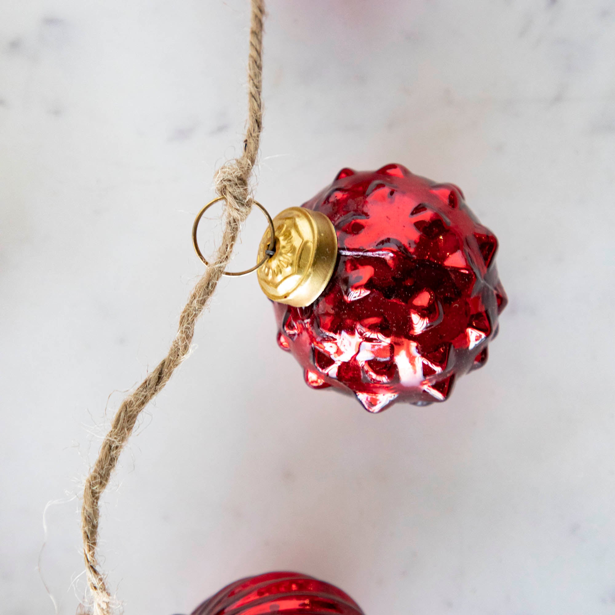 A close up of the Embossed Red Mercury Glass Ball Ornament Garland showing the red spiked detail and jute cord.