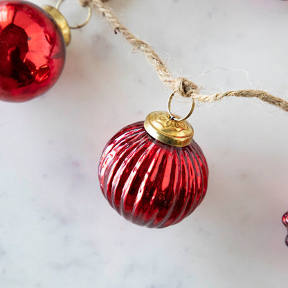 A close up of the Embossed Red Mercury Glass Ornament Garland showing the ribbed detailing and jute cord.