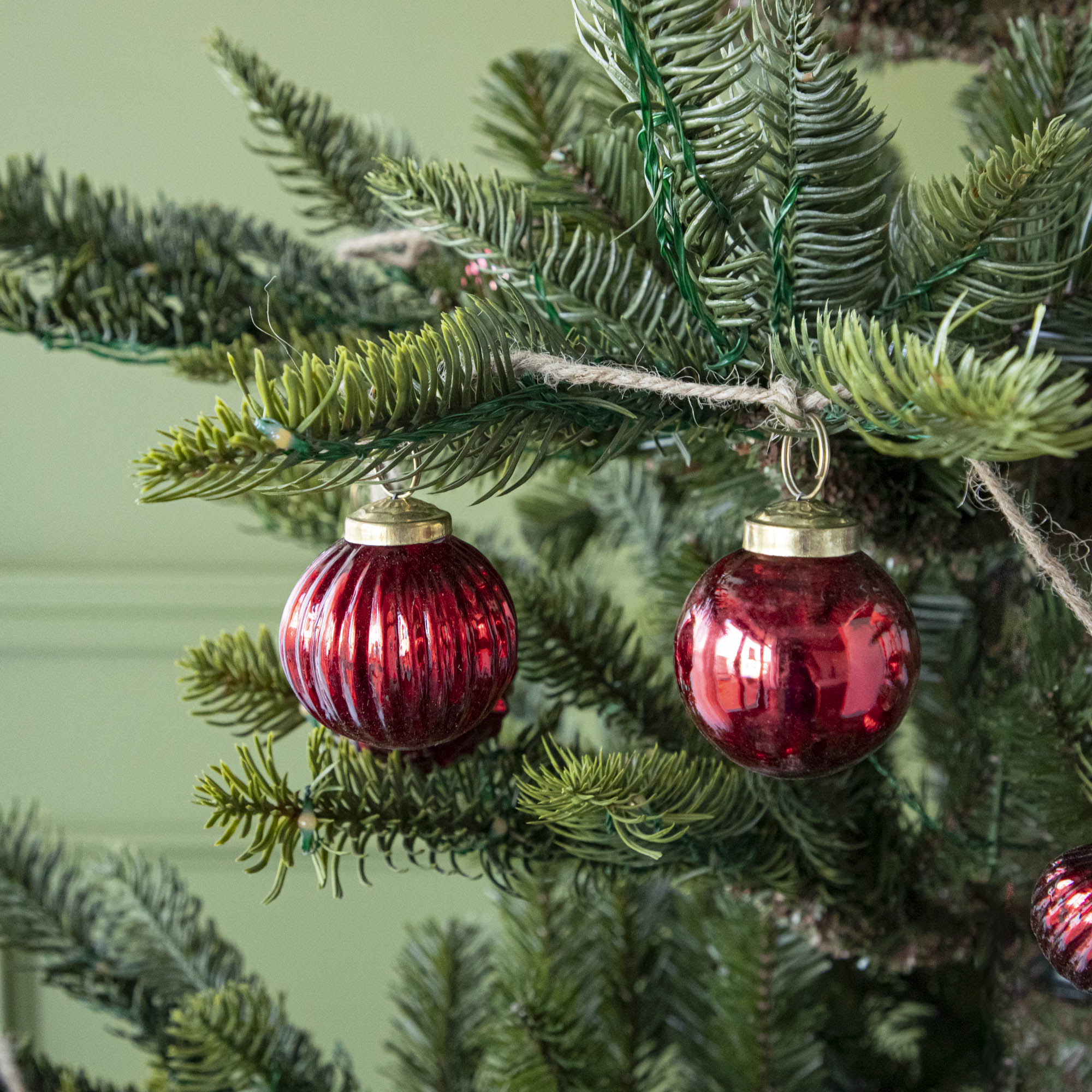 A close up of two Embossed Red Mercury Glass Ornaments showing the detailing and jute cord hanging on a tree.