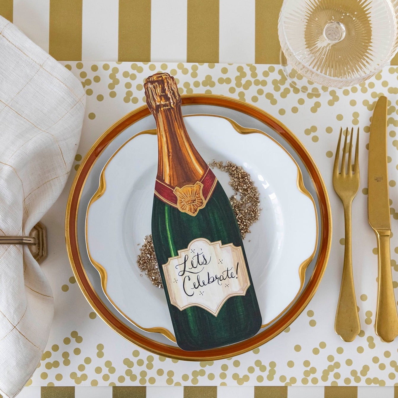 Top-down view of an elegant place setting featuring a Champagne Table Accent with "Let's Celebrate!" written on the label in cursive.