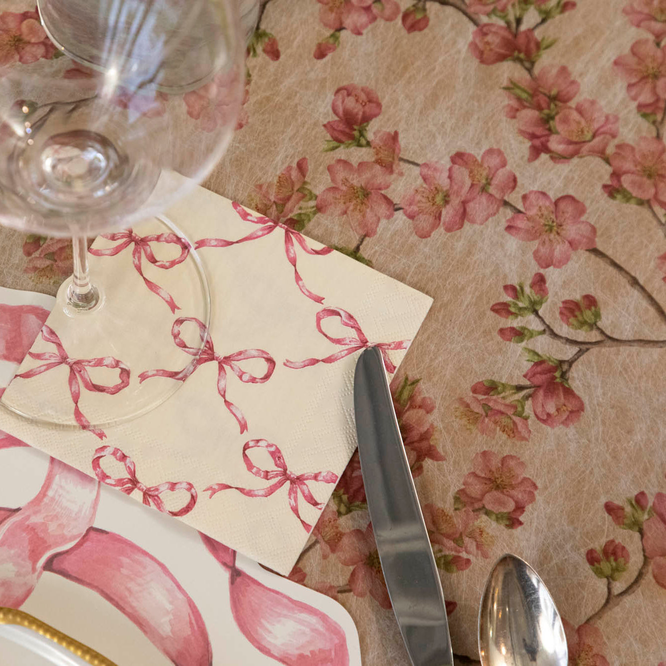 Pink Bow Lattice Cocktail Napkin under a glass behind a place setting.