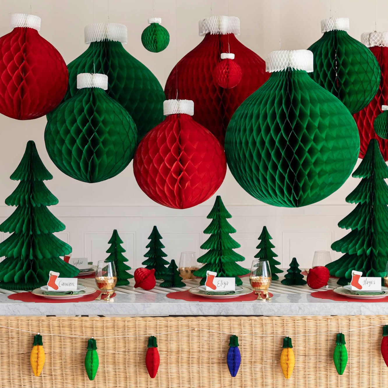 A festive table setting with hanging Honeycomb Large Classic Ornaments, honeycomb trees scattered on the table and Honeycomb Christmas Lights strung on the back of a wicker bench.