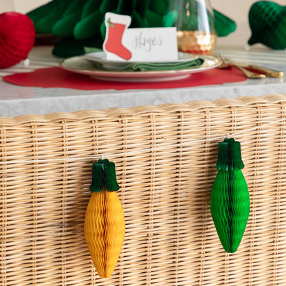 The Honeycomb Christmas Lights in yellow and green, strung on the back of a wicker bench, and a Christmas table setting in the background.